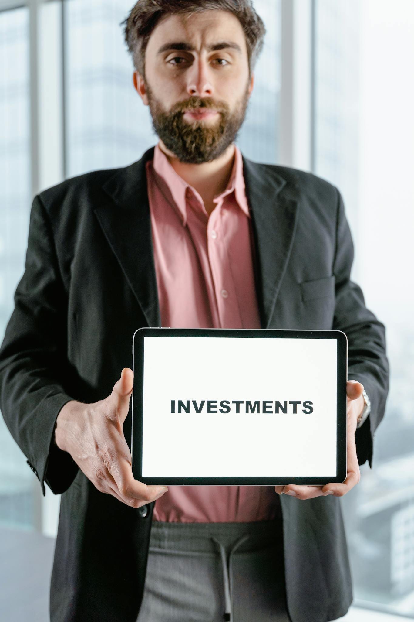 Businessman holding tablet displaying the word 'Investments' in an office setting.